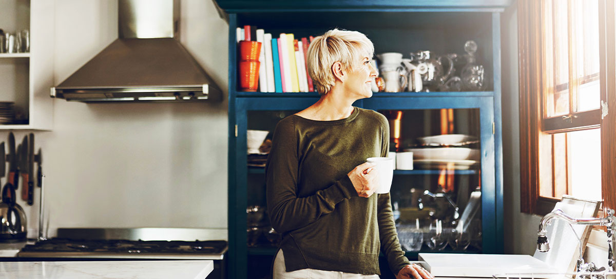 Blonde woman holding a coffee cup looking out her kitchen window	