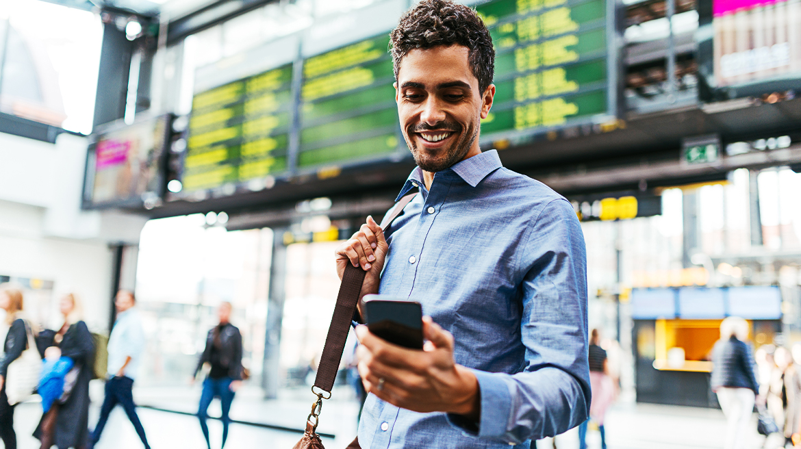 A man carrying a bag looking at his mobile phone and smiling