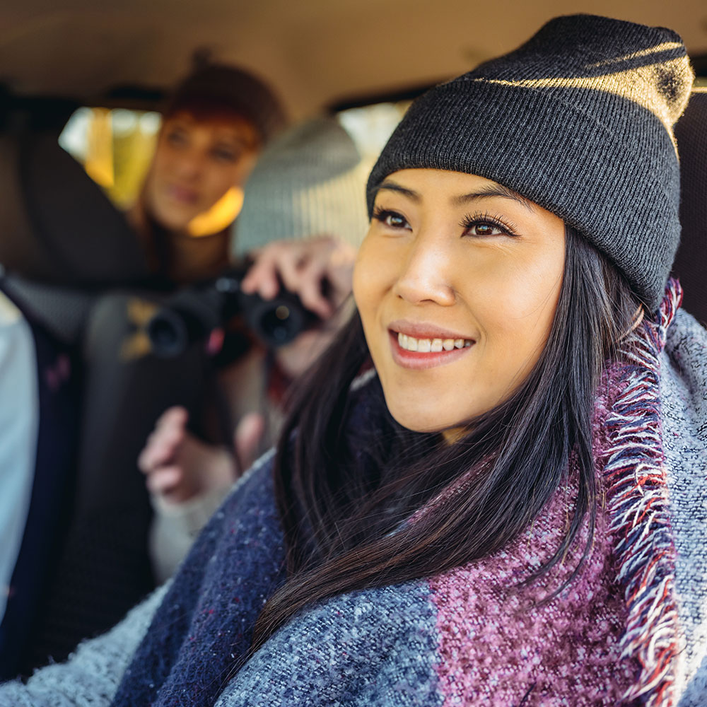 Happy young woman in the driver's seat with friends in the background.