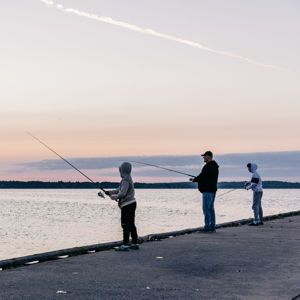 A father and two children fish on the side of a pier.