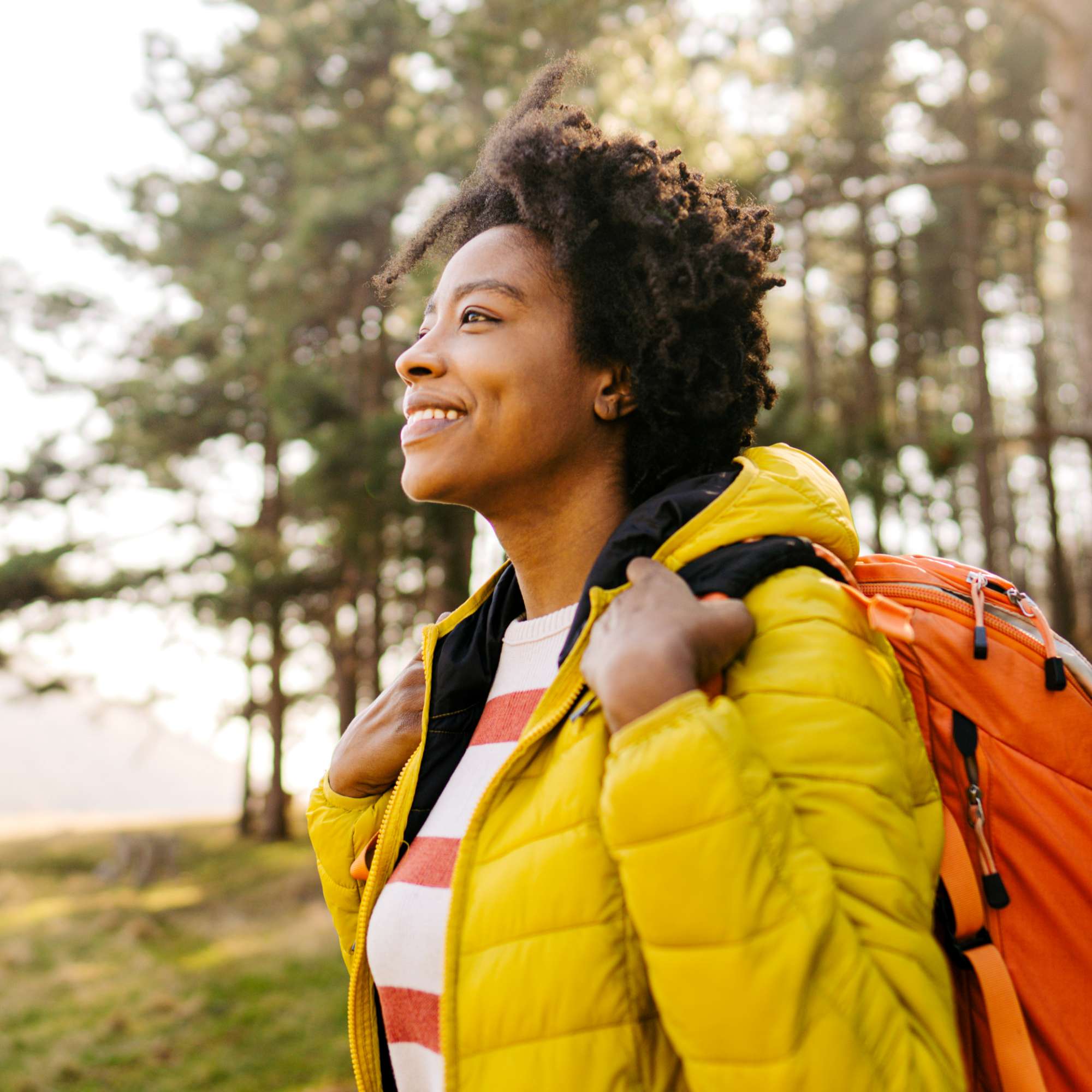 Smiling woman with a backpack, outdoors, wearing a yellow jacket and looking off into the distance