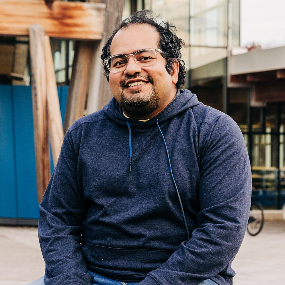 Smiling Meridian Member sitting outside, wearing clear glasses and a blue hooded sweatshirt