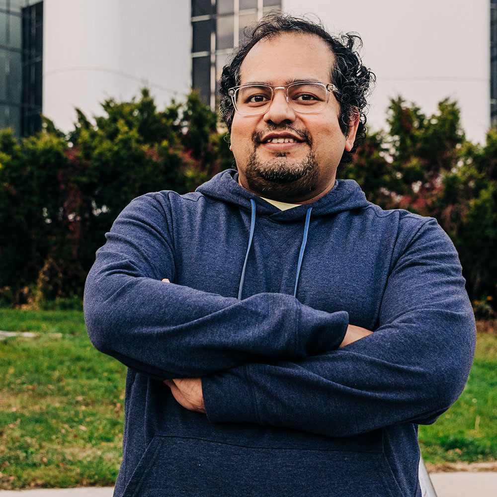 Smiling Meridian Member sitting outside, wearing clear glasses and a blue hooded sweatshirt