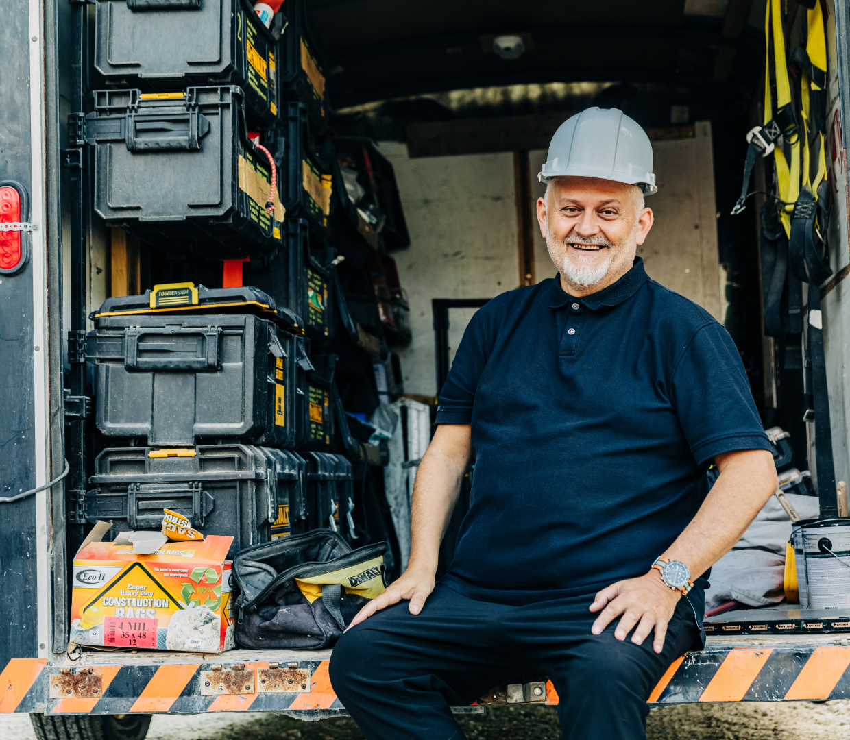 Rob Cikoja - Habitat for Humanity. Rob is sitting on the back of a truck wearing a hard hat. 