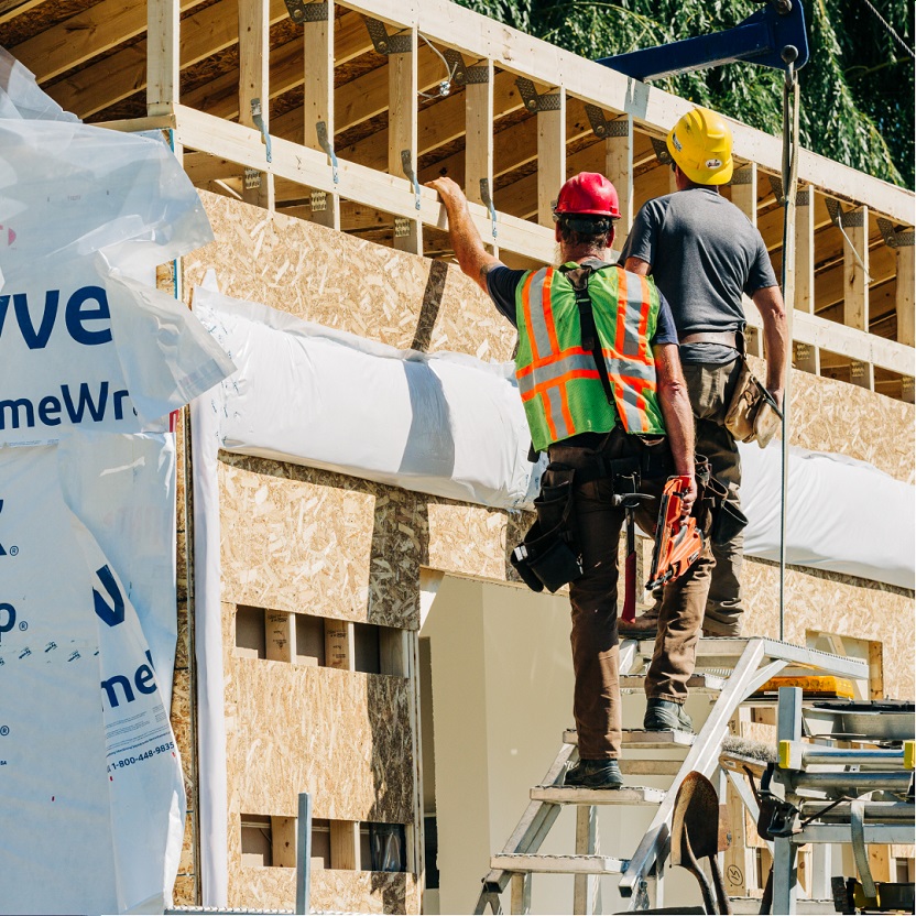 Two male construction workers are standing on a ladder at a new house build