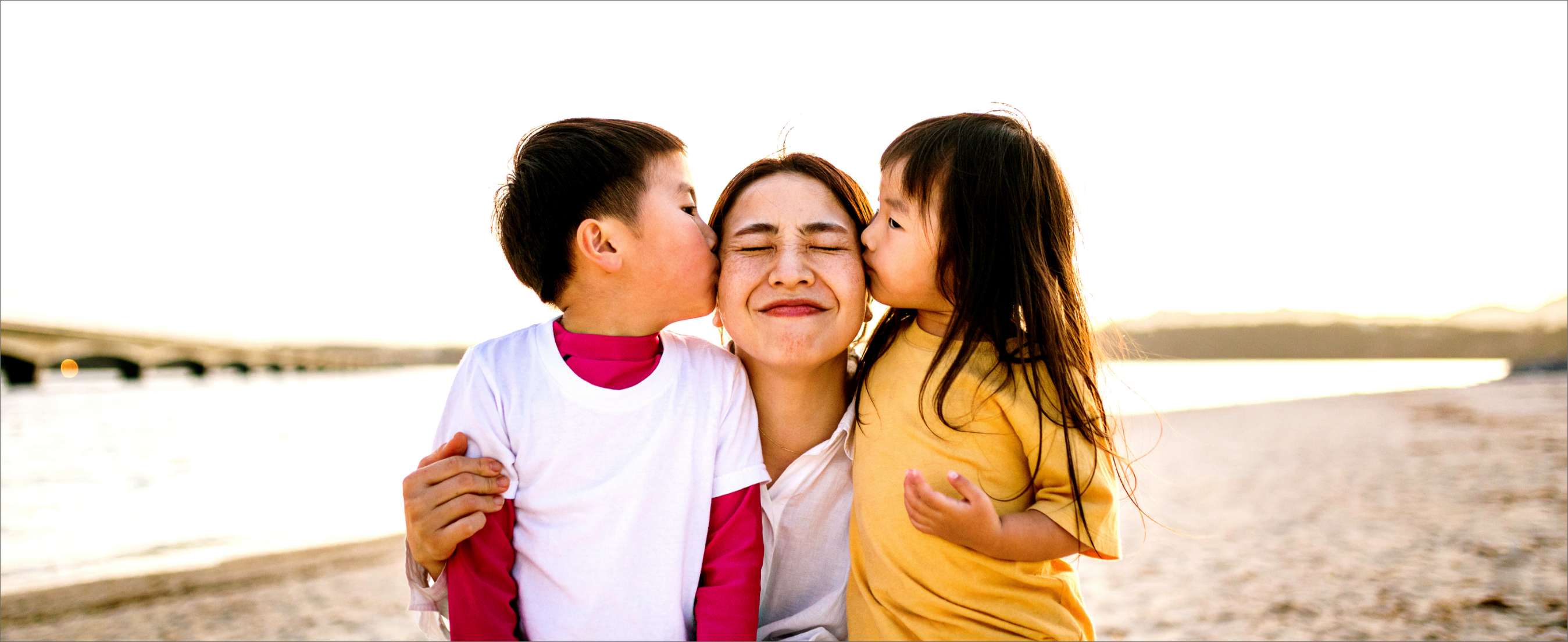 A son and daughter kissing their Asian mother on the cheeks on a beach at dusk