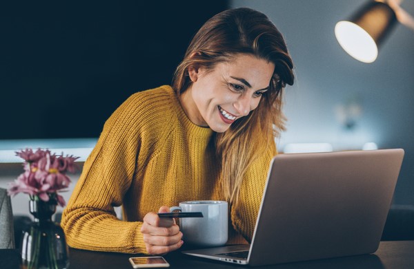 Young woman smiles as she holds a credit card and looks at her laptop.