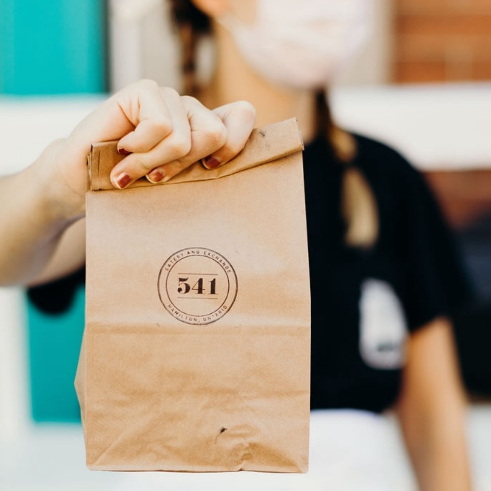 A woman holding a paper bag bearing the 514 Eatery & Exchange logo