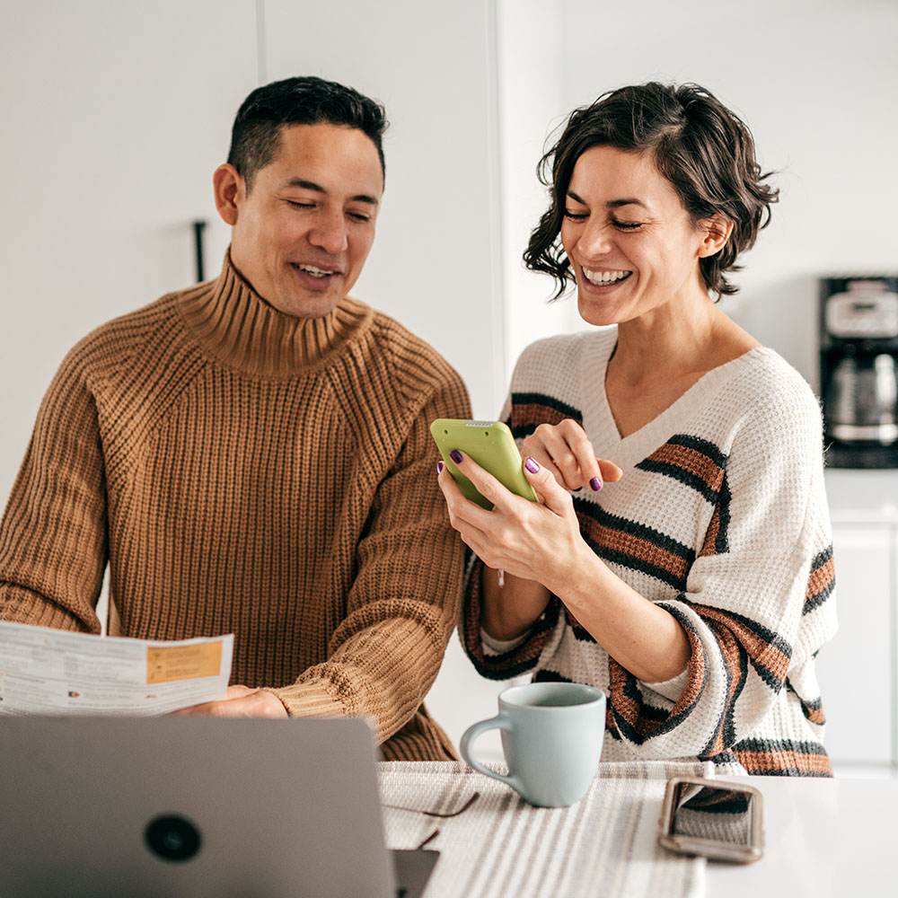 Couple planning their finances in a bright kitchen, using a laptop and smartphone.