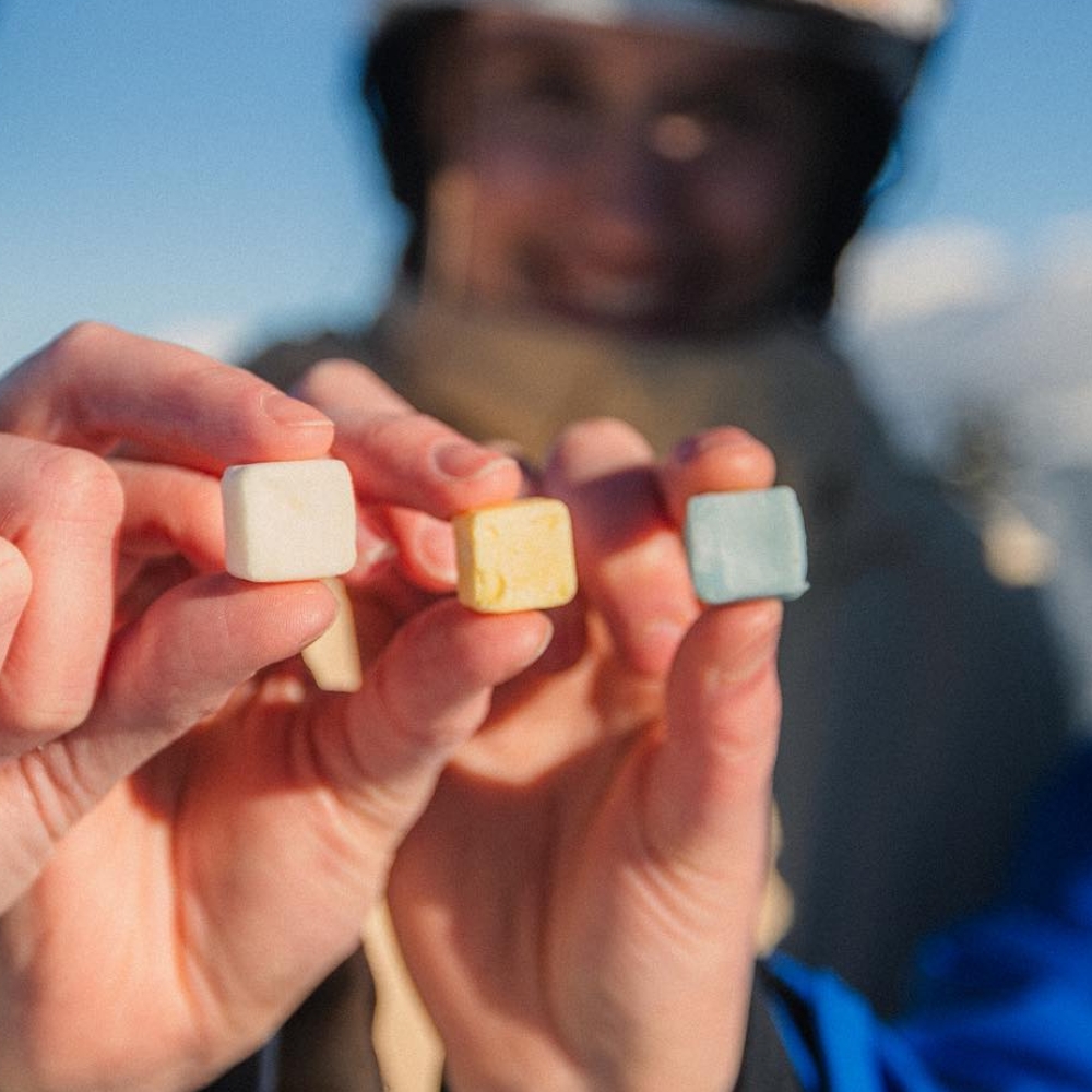 A close up on three hands holding small cubes of colourful EarthSuds products.