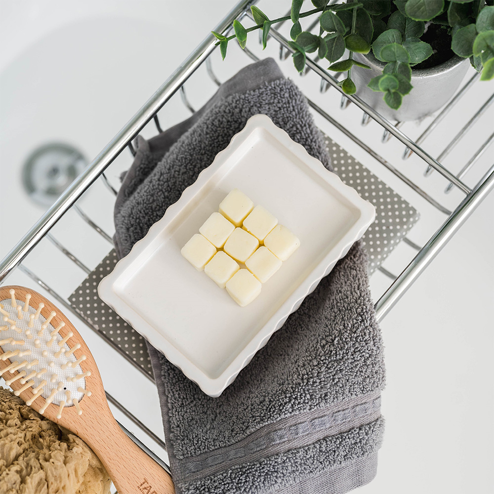 Nine cream coloured soap cubes on a dish. The dish is sitting on a wire bath rack with a towel and brush.