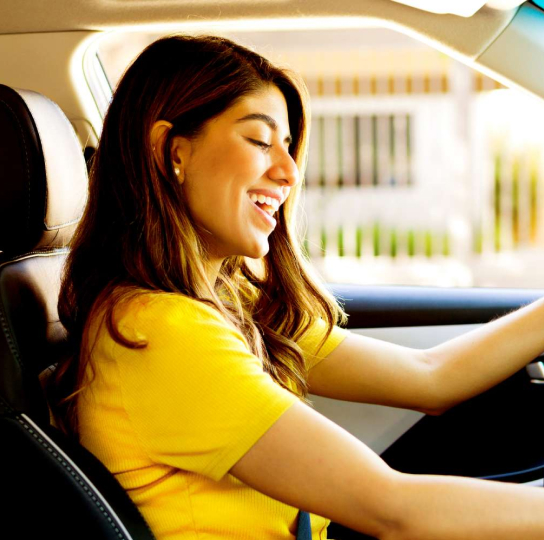 Young woman with medium skin tone and dark hair is smiling as she drives.