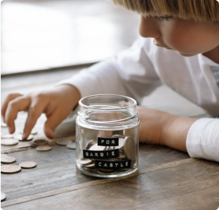 A child puts coins into a jar with a label “for barbie castle”