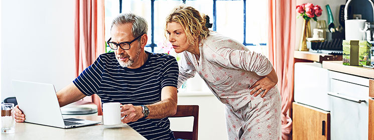 A middle-aged couple are in their kitchen wearing pajamas, looking intently at a laptop.A middle-aged couple are in their kitchen wearing pajamas, looking intently at a laptop.