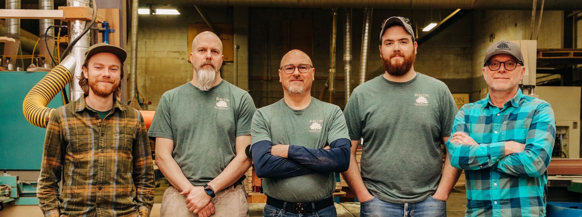 A group of five male employees of Byrcon Wood Products, standing with their arms crossed in a warehouse, looking confident and determined.