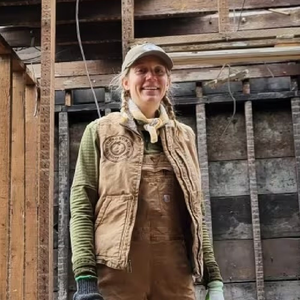 A woman in an Ouroboros-branded vest standing in a home deconstruction site.