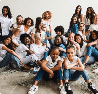 A diverse group of smiling women and girls, all wearing jeans and white t-shirts