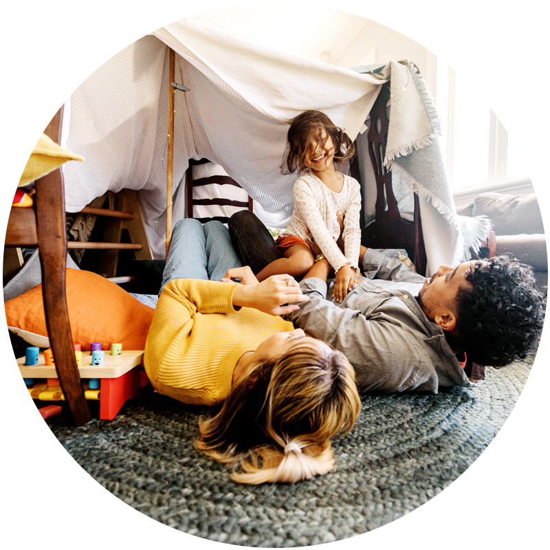 Family playing together inside a cozy blanket fort at home.