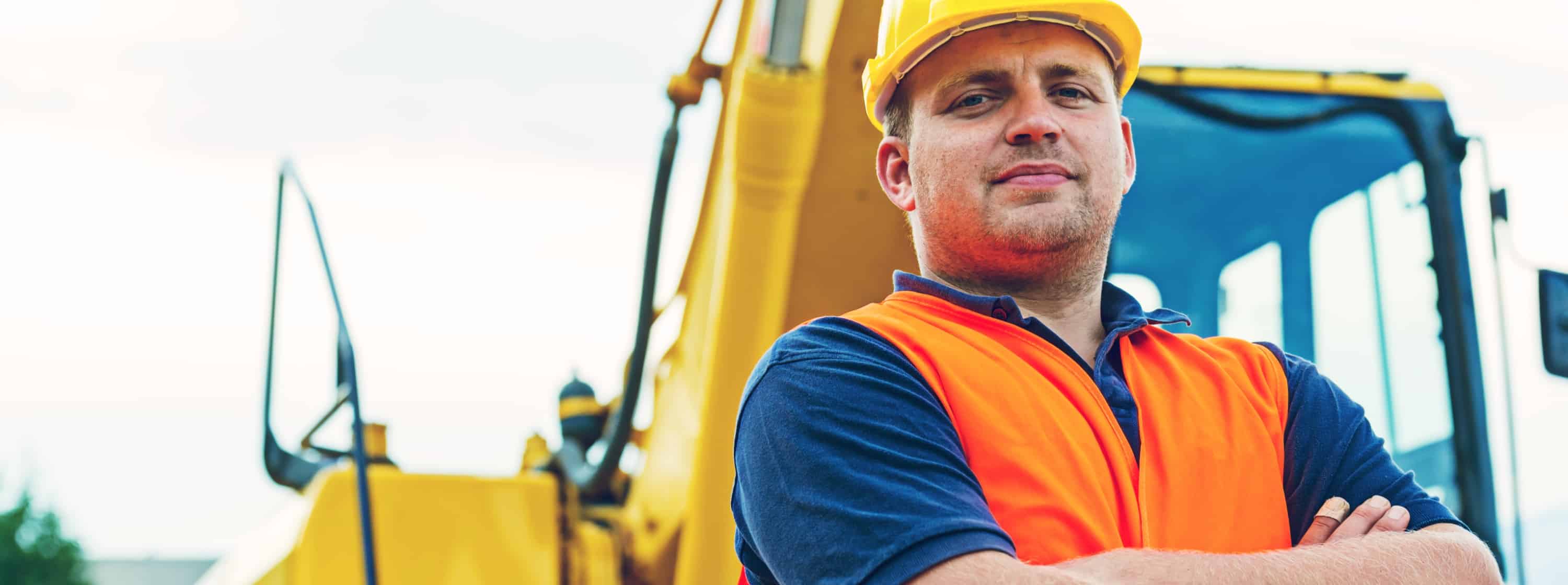A construction worker in a yellow helmet standing in front of construction equipment