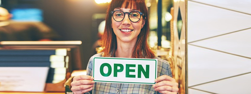 Female business owner, smiling, holding a sign that says, open.