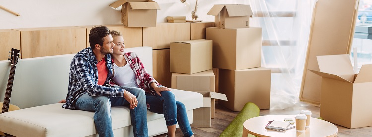 Young couple sitting on their couch, relaxing, surrounded by moving boxes